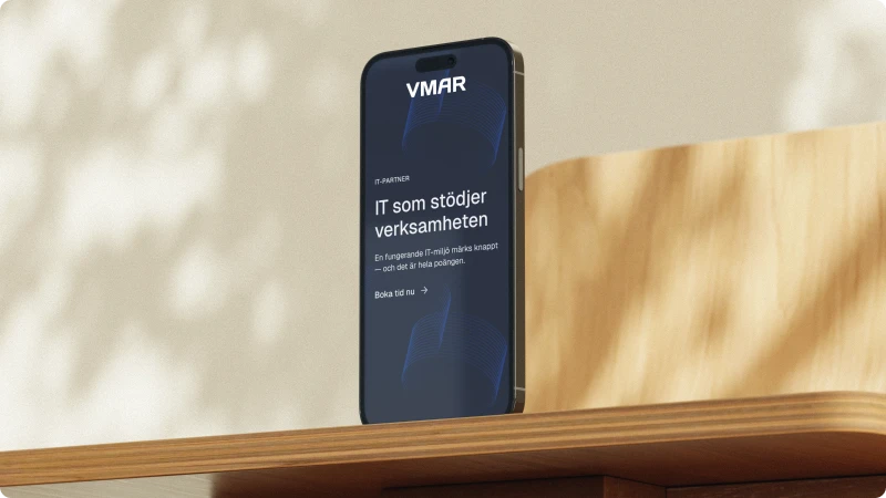 Stående mobiltelefon placerad på ett träbord med VMAR:s webbplats öppen på skärmen.